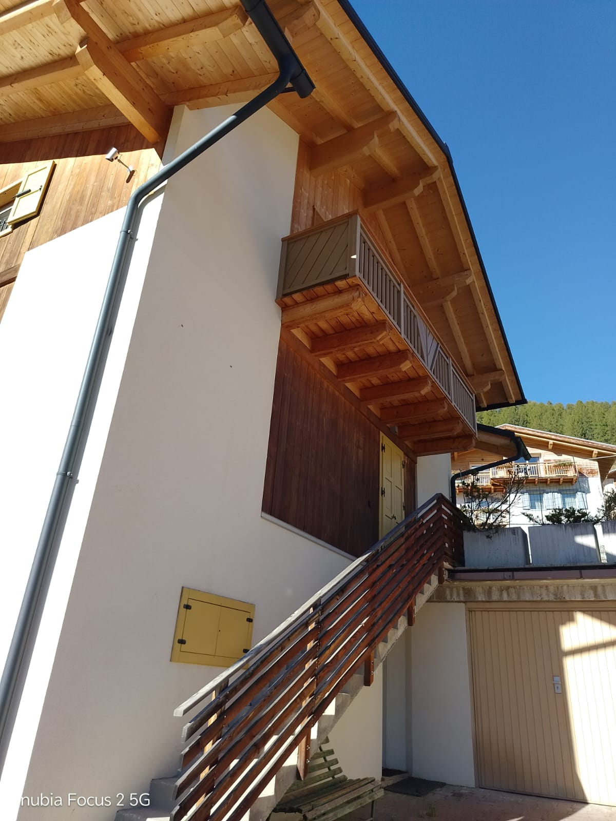 A white-and-wood building exterior with a staircase, balconies, roof overhangs, and strong sunlight.